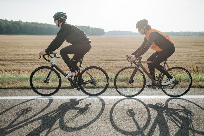 Two road cyclists riding side by side past a harvested field on a rural German road