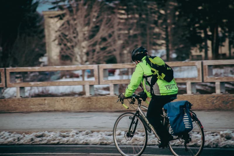Commuter in a high-visibility jacket riding past snow on a winter road